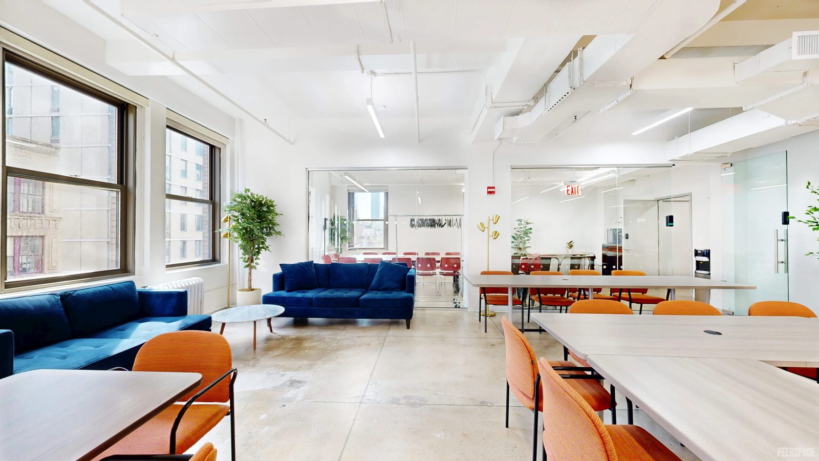 Luma Studios: a bright open floor with blue sofas, long tables and orange chairs by tall windows.